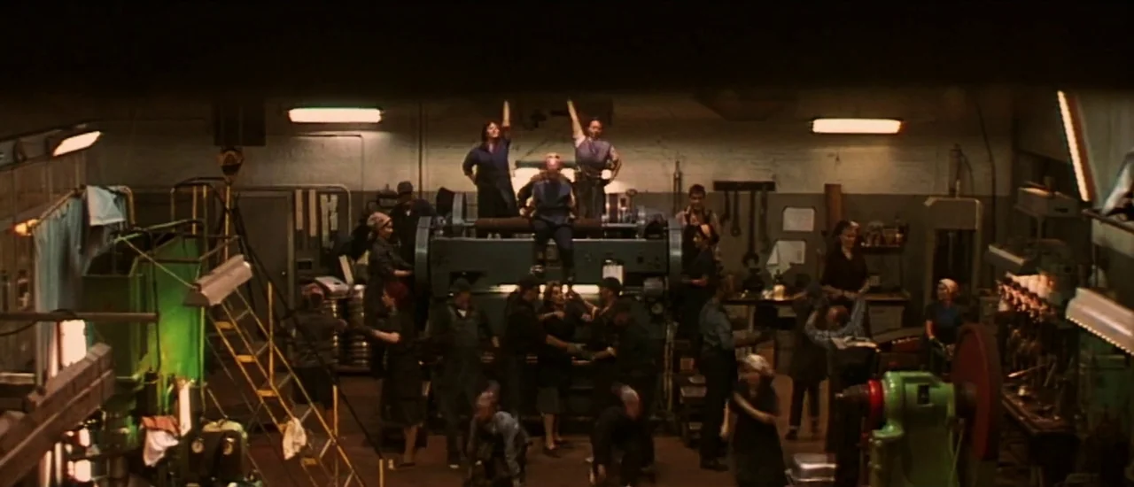 Dancer in the Dark (2000) movie still: wide — A bustling 1940s industrial floor filled with heavy machinery and diverse workers. The group moves…