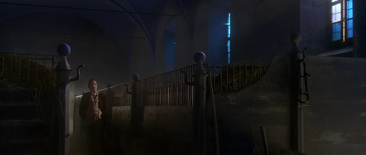 The Portait of a Lady (1996) movie still: wide — A dark, cavernous interior with wooden stalls filled with loose hay. A lone man stands in the aisle…
