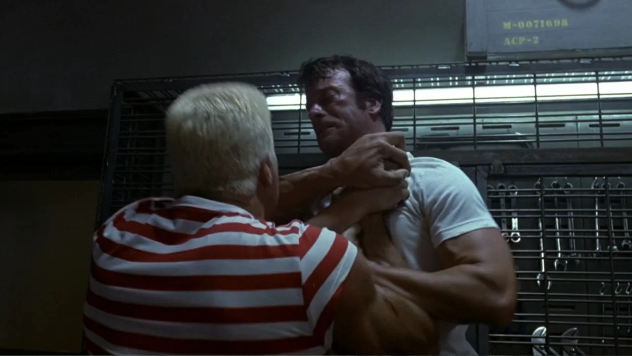 The Punisher (2004) movie still: medium — A cramped industrial space features a metal grid wall filled with hanging metal tools. Two muscular men…