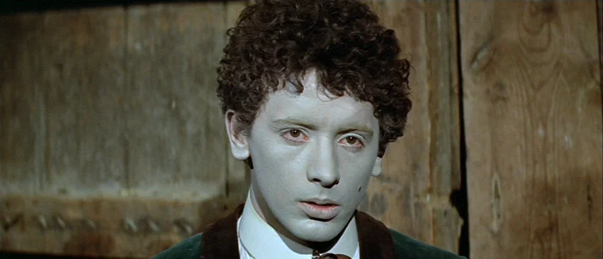 Whity (1971) movie still: closeup — A close portrait shows a person against a background of aged, vertical wooden planks. The man has thick curly…
