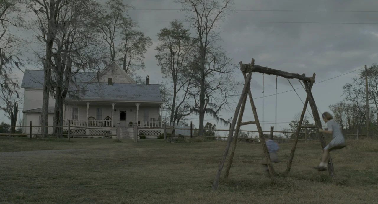 The Green Mile (1999) movie still: wide — A rustic wooden swing set sits in a vast field before an old farmhouse. Two children sway on the swing set…