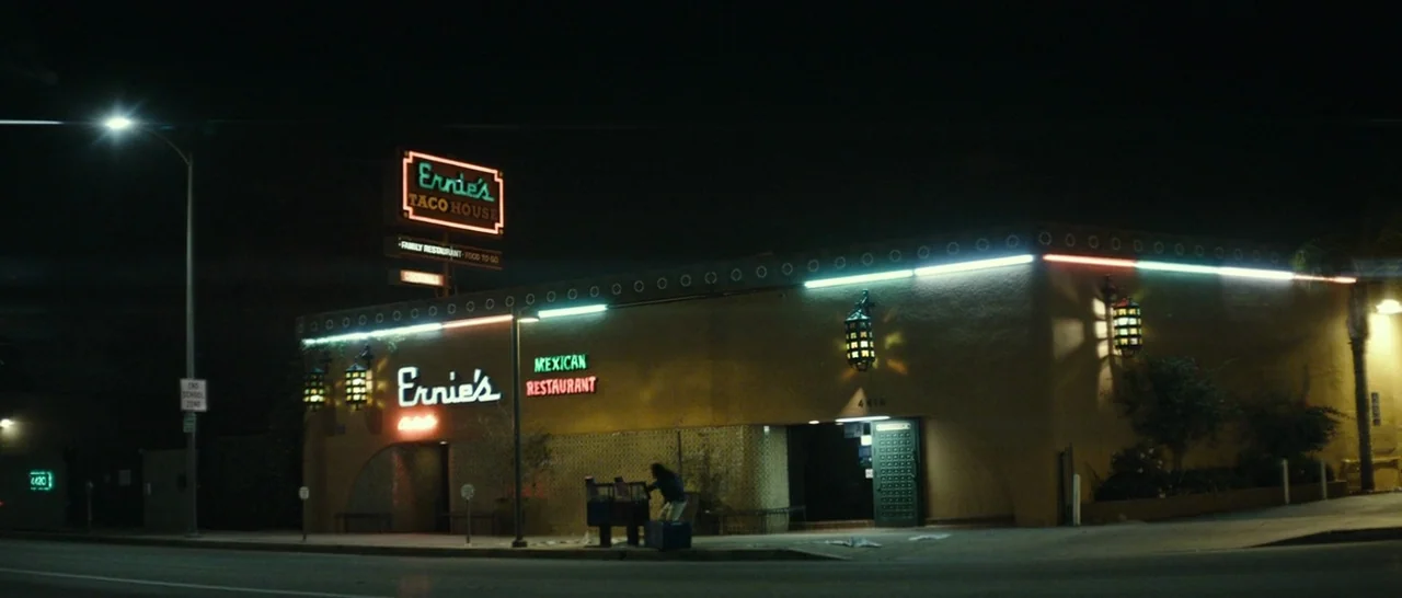 The Disaster Artist (2017) movie still: establishing — A low-rise Mexican restaurant building at night features glowing neon signage and lanterns. A…