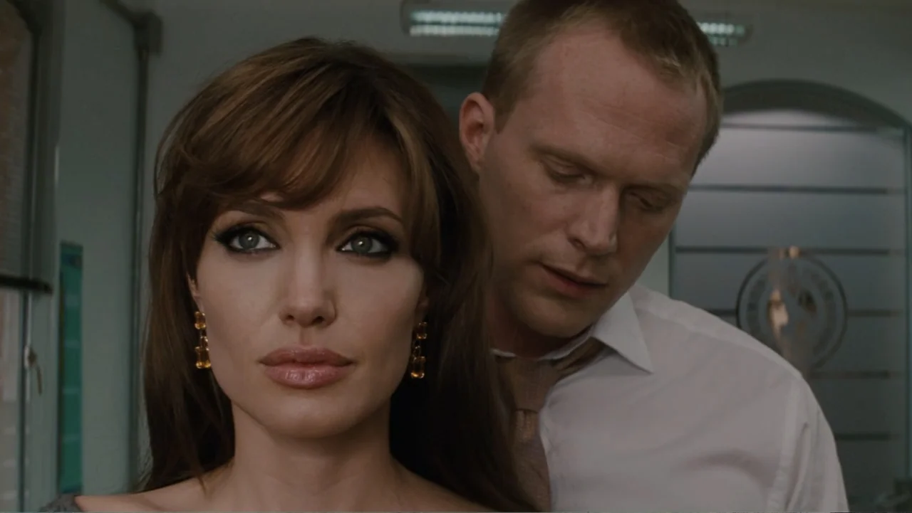 The Tourist (2010) movie still: medium — A modern interior office space with a blurred glass door in the background. A woman stands in the…