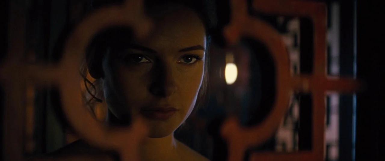 Mission: Impossible – Rogue Nation (2015) movie still: closeup — A woman looks through the opening of a decorative carved dark wooden partition. The…