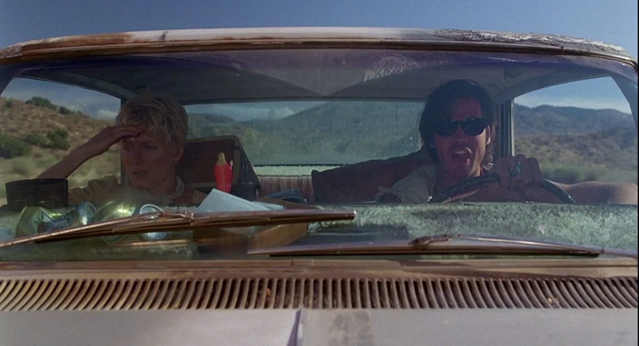 Psycho III (1986) movie still: medium — A convertible travels through a dry, mountainous desert landscape on a sunny day. A woman and a man drive…