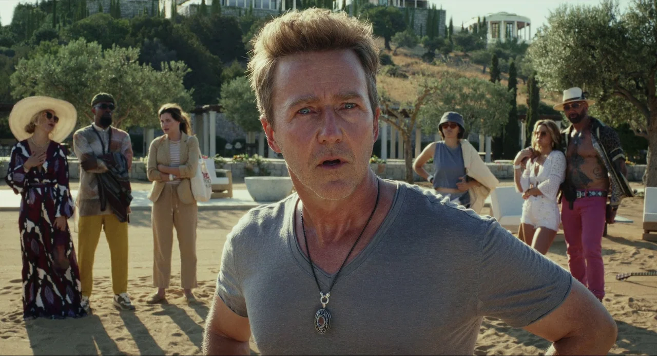 Glass Onion (2022) movie still: medium — A group of six people stands in a sunlit open courtyard area with olive trees. A man in the foreground…