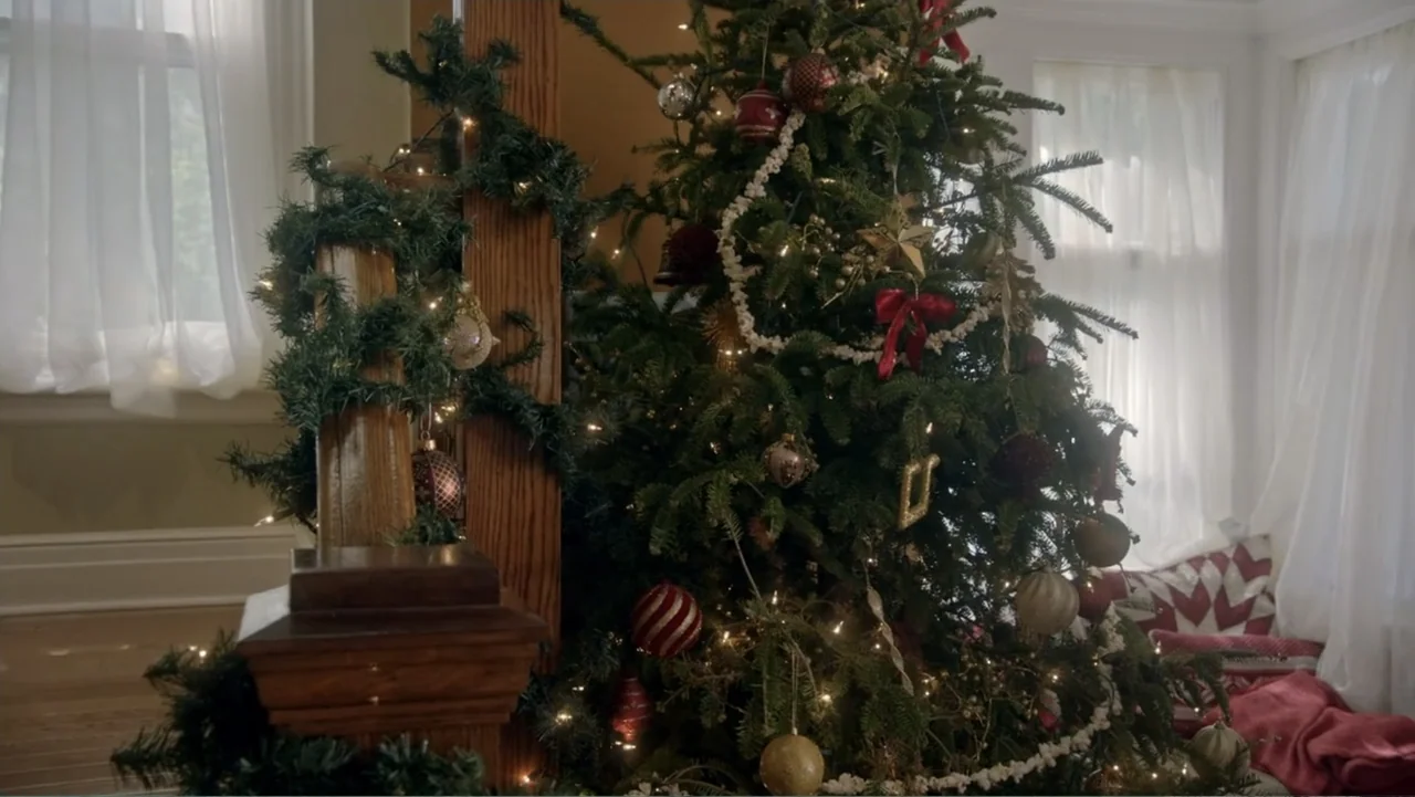 The Christmas Cure (2017) movie still: medium — A decorated Christmas tree sits indoors next to a wooden staircase post. Natural light shines…