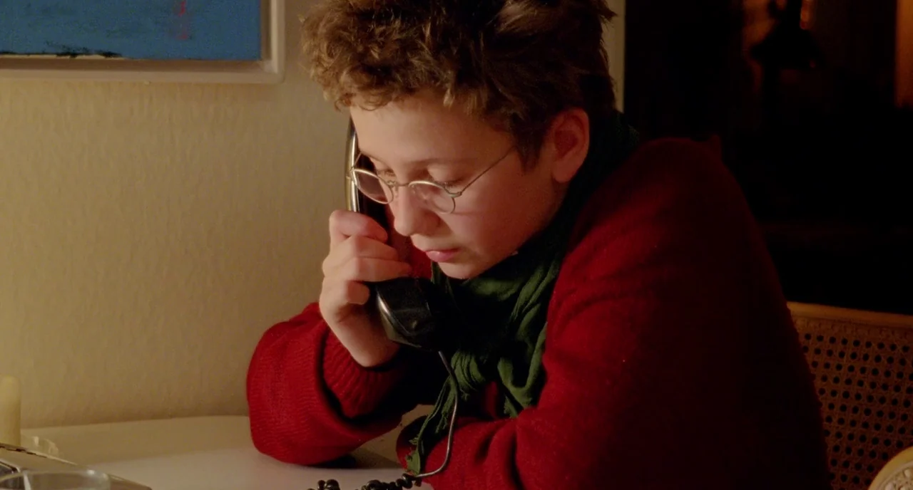 We Are The Best! (2013) movie still: medium — A person sits at a desk illuminated by warm light at night. They hold a black corded telephone handset…