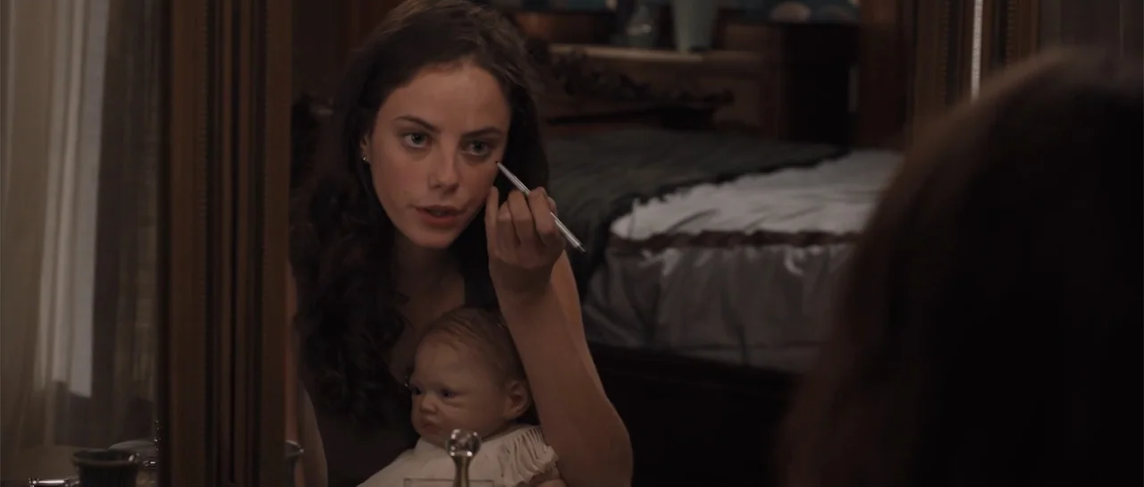 The Truth About Emanuel (2013) movie still: medium — A woman sits before a large mirror in a bedroom with a bed behind her. She holds a realistic…