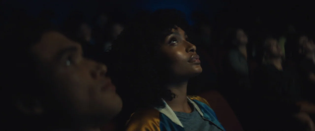The Sun Is Also a Star (2019) movie still: medium — A dark movie theater interior with rows of seats occupied by viewers. A young woman and a young…