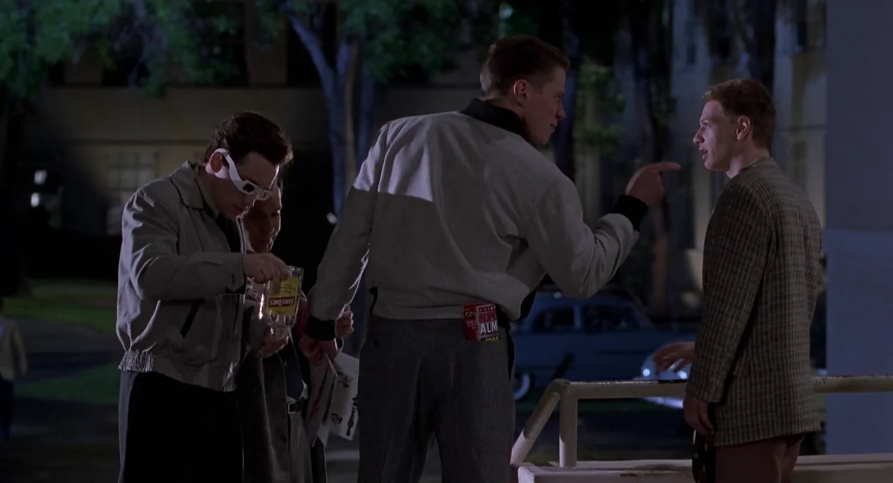 Back to the Future II (1989) movie still: fullbody — A dark outdoor area at night with trees and a parked classic car. Three men stand together in…