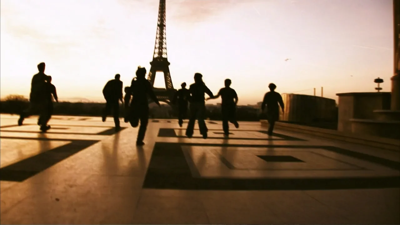 28 Weeks Later (2007) movie still: wide — A stone-tiled public square features an iconic iron tower in the distant background. A group of several…