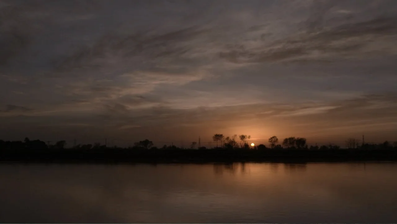 A Girl in the River: The Price of Forgiveness (2015) movie still: establishing — A wide river flows horizontally across the frame under a cloudy…