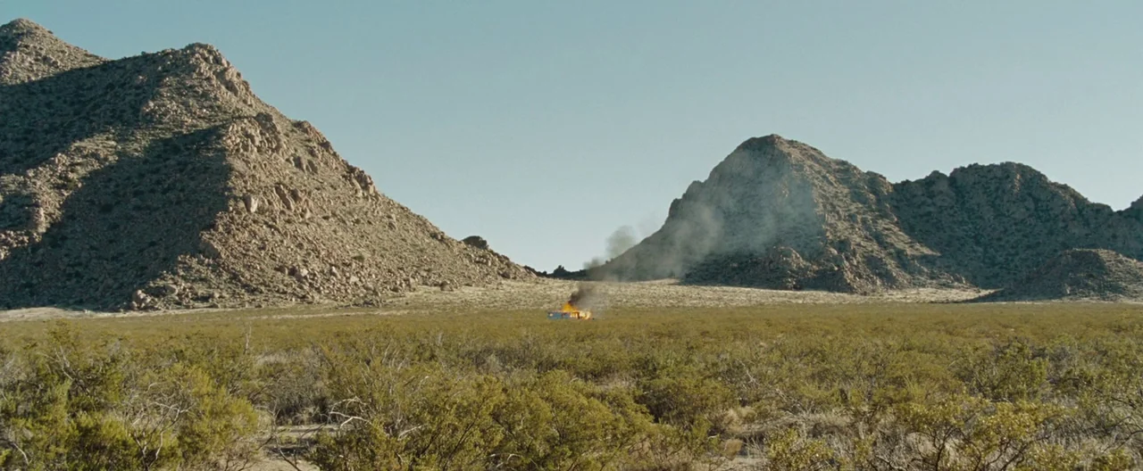 The Burning Plain (2008) movie still: establishing — A desolate desert landscape framed by large, rocky mountains under a clear blue sky. A small…