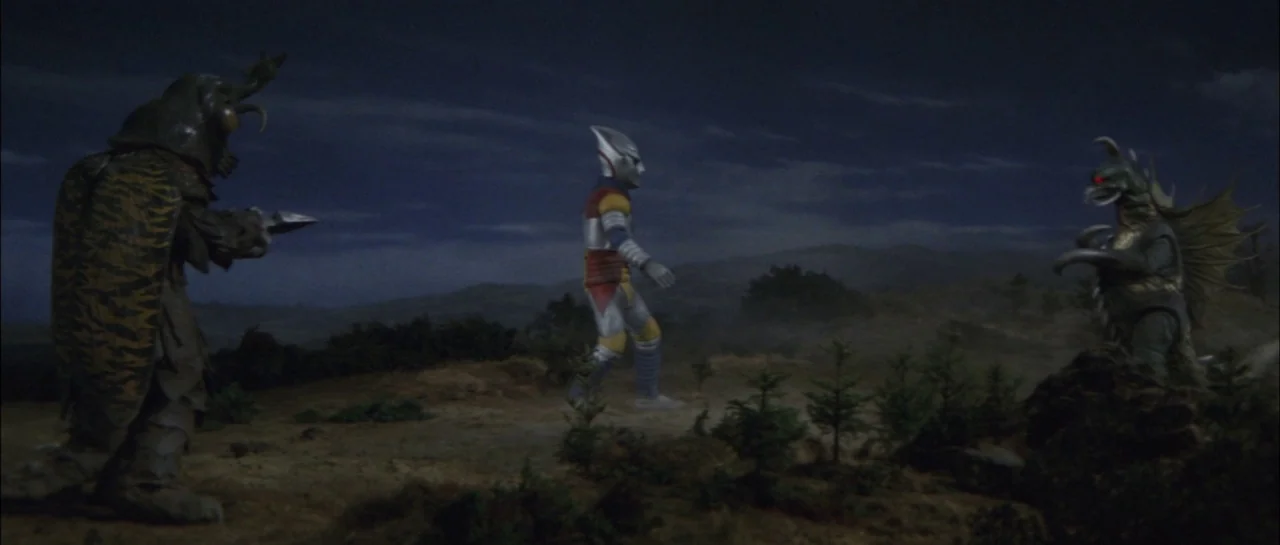 Godzilla Vs Megalon (1973) movie still: wide — A desolate rocky plain is illuminated under a dark night sky with sparse pine trees. Three costumed…