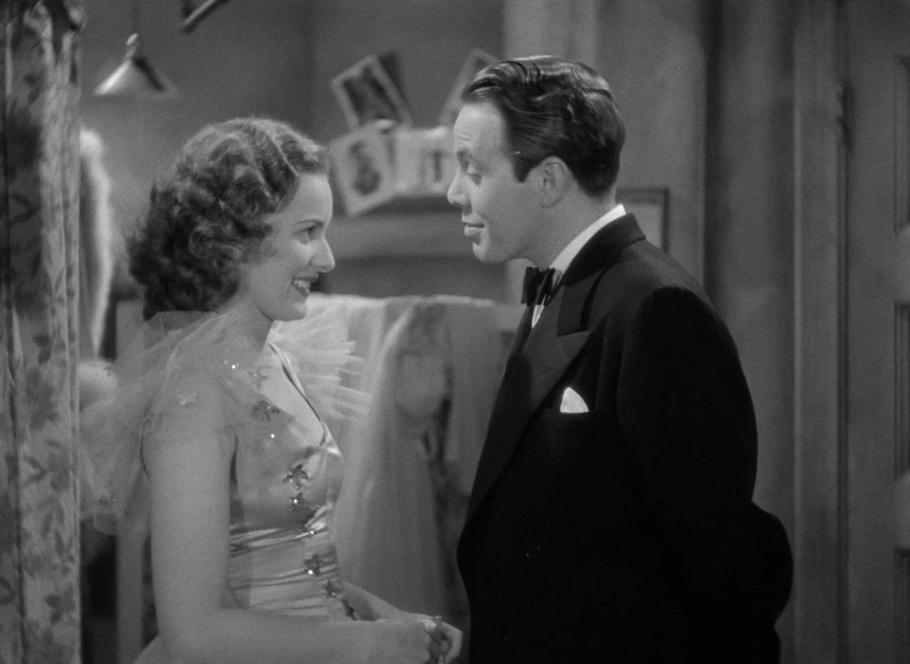 Dance, Girl, Dance (1940) movie still: medium — A cramped dressing room contains racks of clothes and personal photos hanging on walls. A man in a…