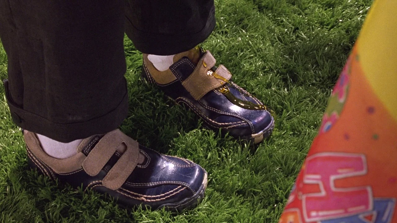 Seed of Chucky (2004) movie still: closeup — Synthetic green grass provides a base for feet wearing dark blue velcro shoes. A viscous substance…