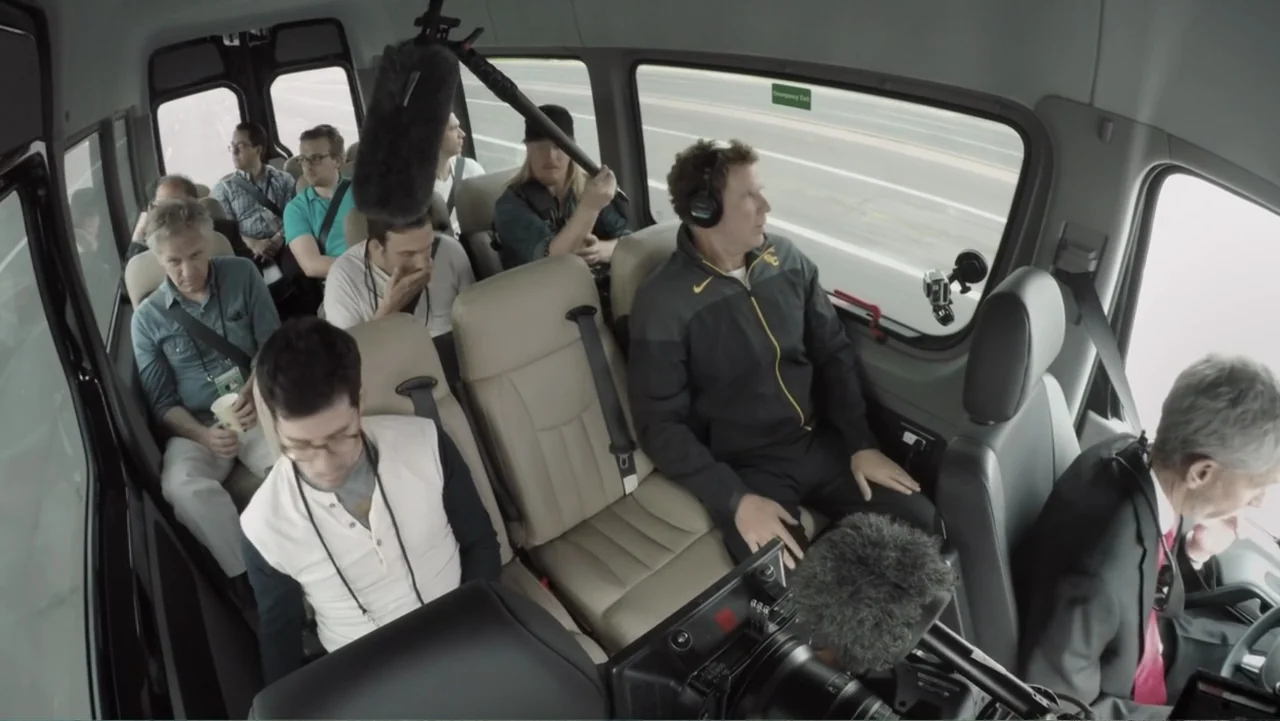 Ferrell Takes the Field (2015) movie still: wide — The interior of a passenger van shows several people seated in beige leather chairs. A crew…