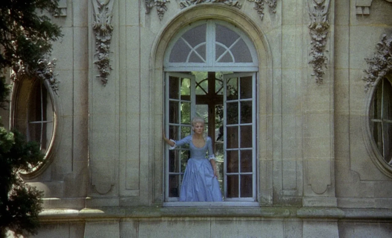 The Beast (1975) movie still: wide — A stone manor facade features ornate carvings and a central open window. A woman stands in the center of the…