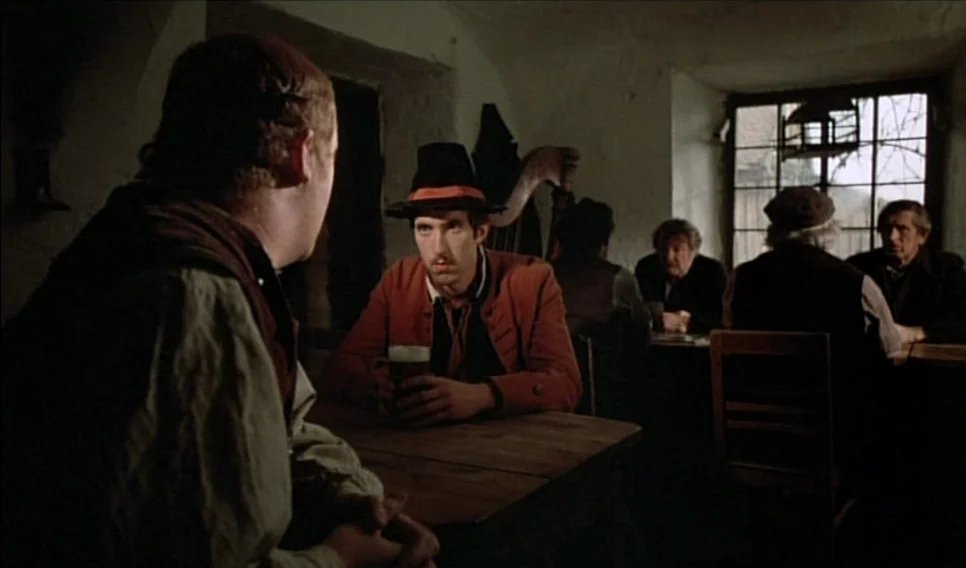 Heart of Glass (1976) movie still: medium — A dimly lit room with stone walls and a paneled window looking outdoors. Several men sit at wooden…