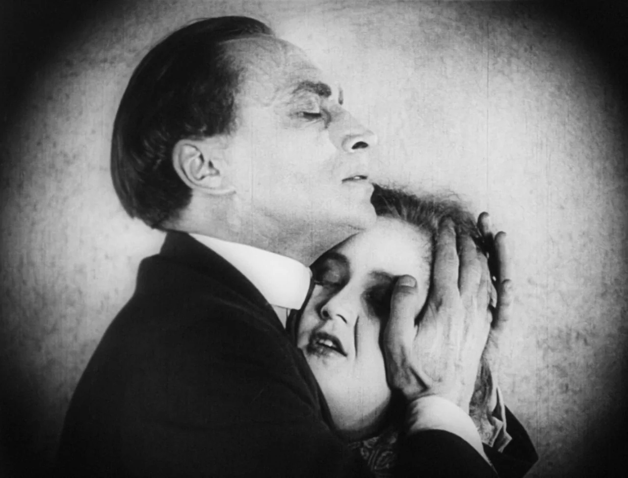 The Hands of Orlac (1924) movie still: closeup — A plain interior background with heavy circular vignetting surrounding the figures. A man clutches…