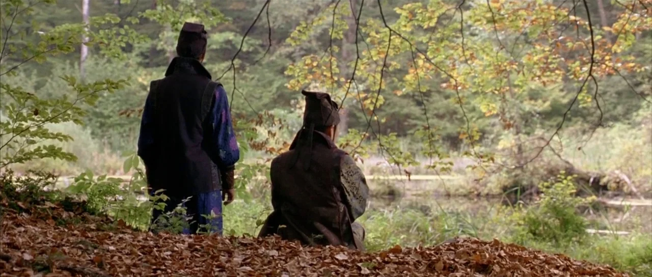 House of Flying Daggers (2004) movie still: fullbody — A dense woodland clearing contains a small pond bordered by fallen autumn leaves. Two figures…