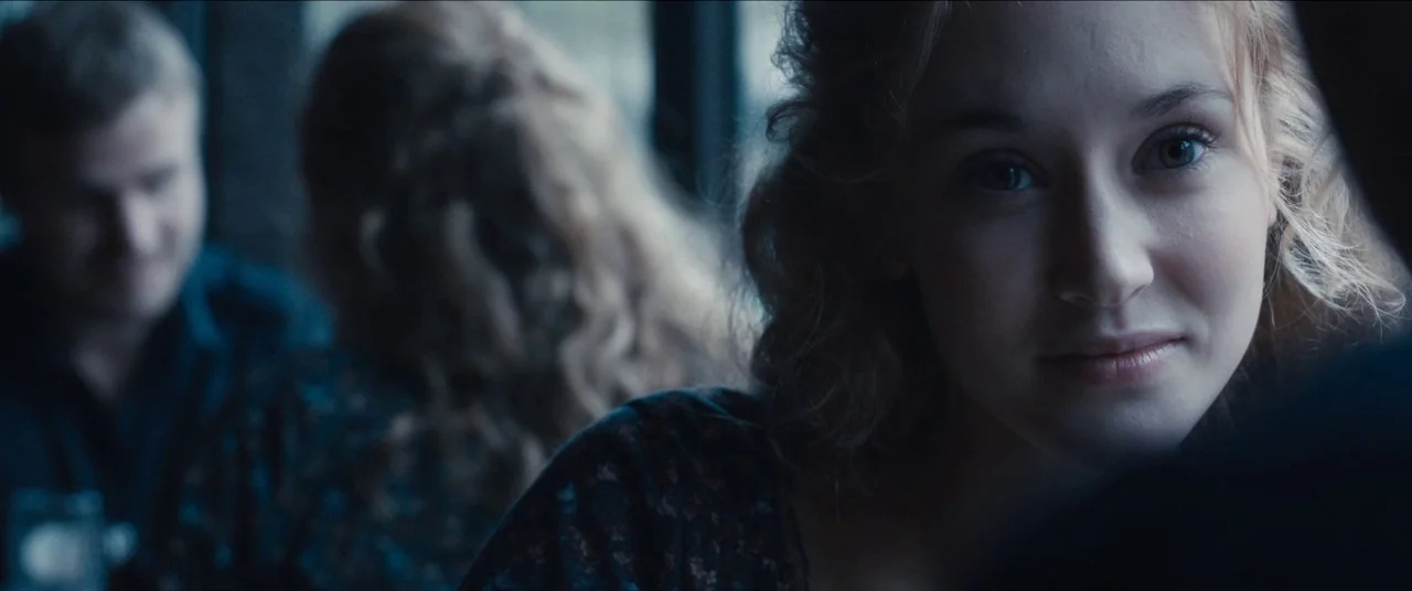 Simon Killer movie still: closeup — A passenger train car interior with window light highlighting the passengers. A young woman with wavy hair looks…