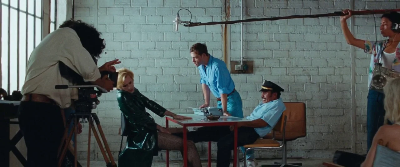 Knife+Heart (2018) movie still: wide — A utilitarian industrial space with white painted brick walls and a large side window. Crew members film a…