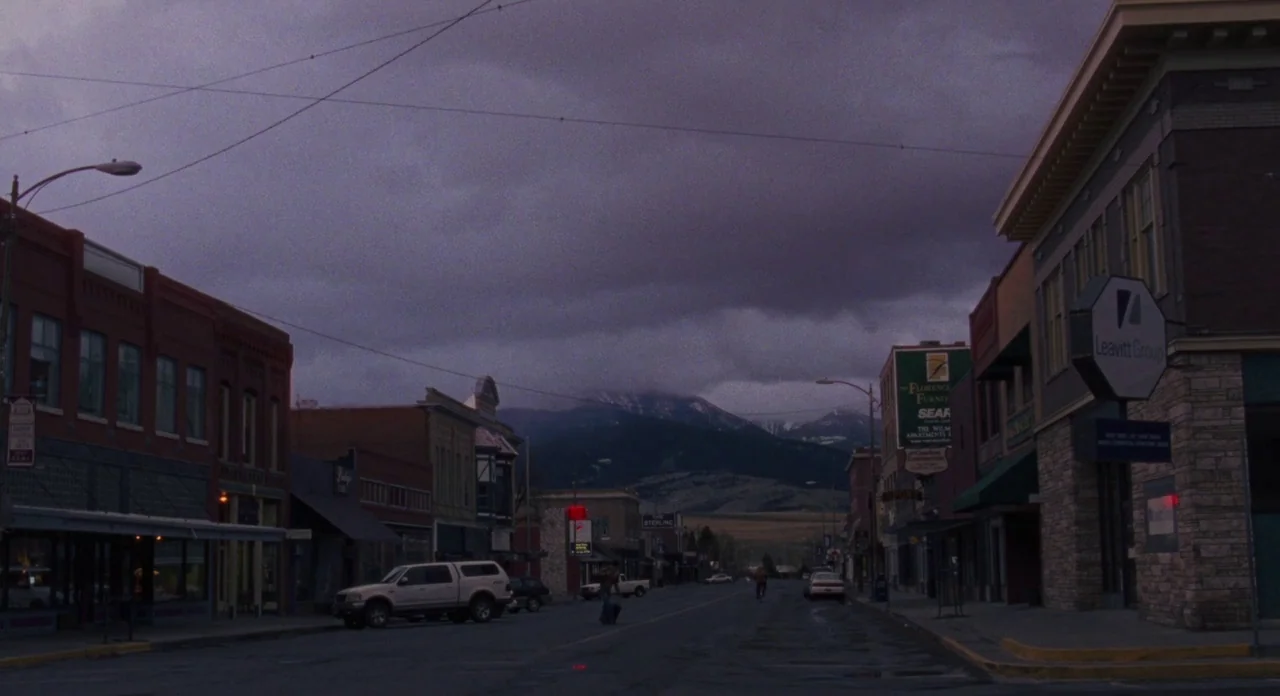 Certain Women (2016) movie still: establishing — A small-town main street stretches into the distance toward a large, dark mountain range. Low-rise…