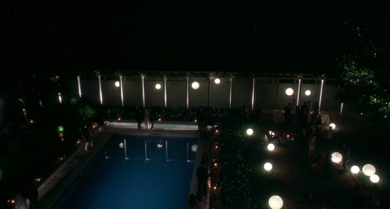 Making of: I Am Love (2009) movie still: establishing — A nighttime backyard pool area is decorated with glowing spherical lanterns and wall…