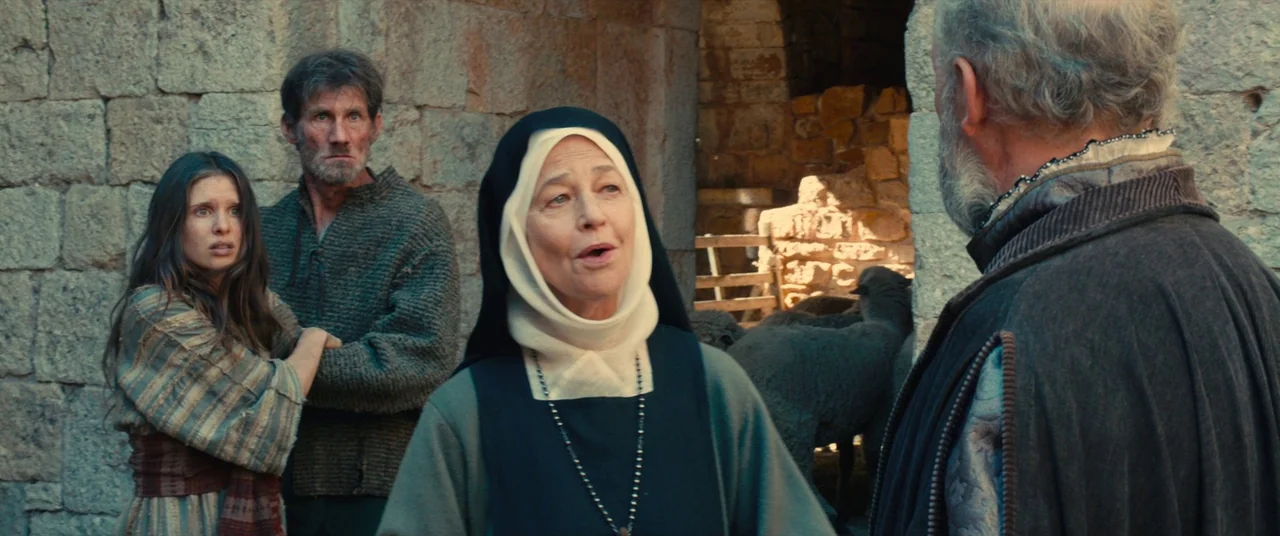 Benedetta (2021) movie still: medium — A stone courtyard with rustic architecture features several individuals gathered during daylight. An elderly…