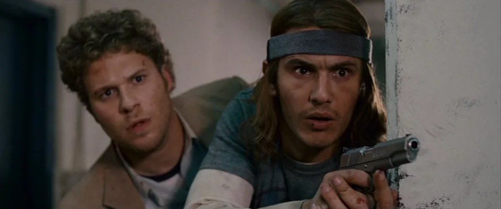 Pineapple Express (2008) movie still: medium — An interior hallway with off-white walls features two men peaking around a corner. One man points a…