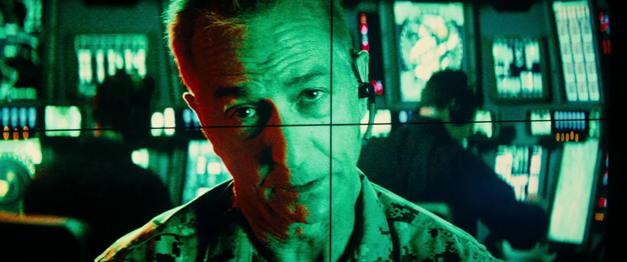 Godzilla: King of the Monsters (2019) movie still: closeup — A dark military operations center is filled with multiple glowing monitors displaying…