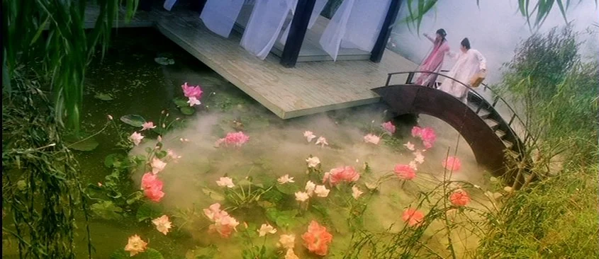 Green Snake (1993) movie still: wide — A lotus pond is covered in low-lying fog with an arched bridge crossing it. Two figures in traditional…