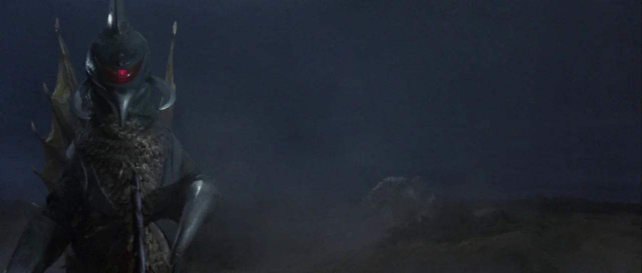 Godzilla Vs Gigan (1972) movie still: medium — A dark, desolate plain stretches out under a night sky with low-hanging atmospheric haze. A large…