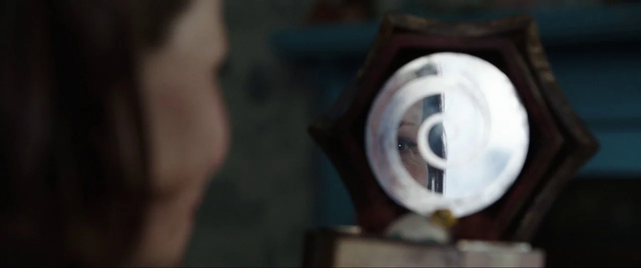 The Conjuring (2013) movie still: closeup — A dark indoor space where a person holds a small ornate hexagonal mirror. The mirror surface reflects a…