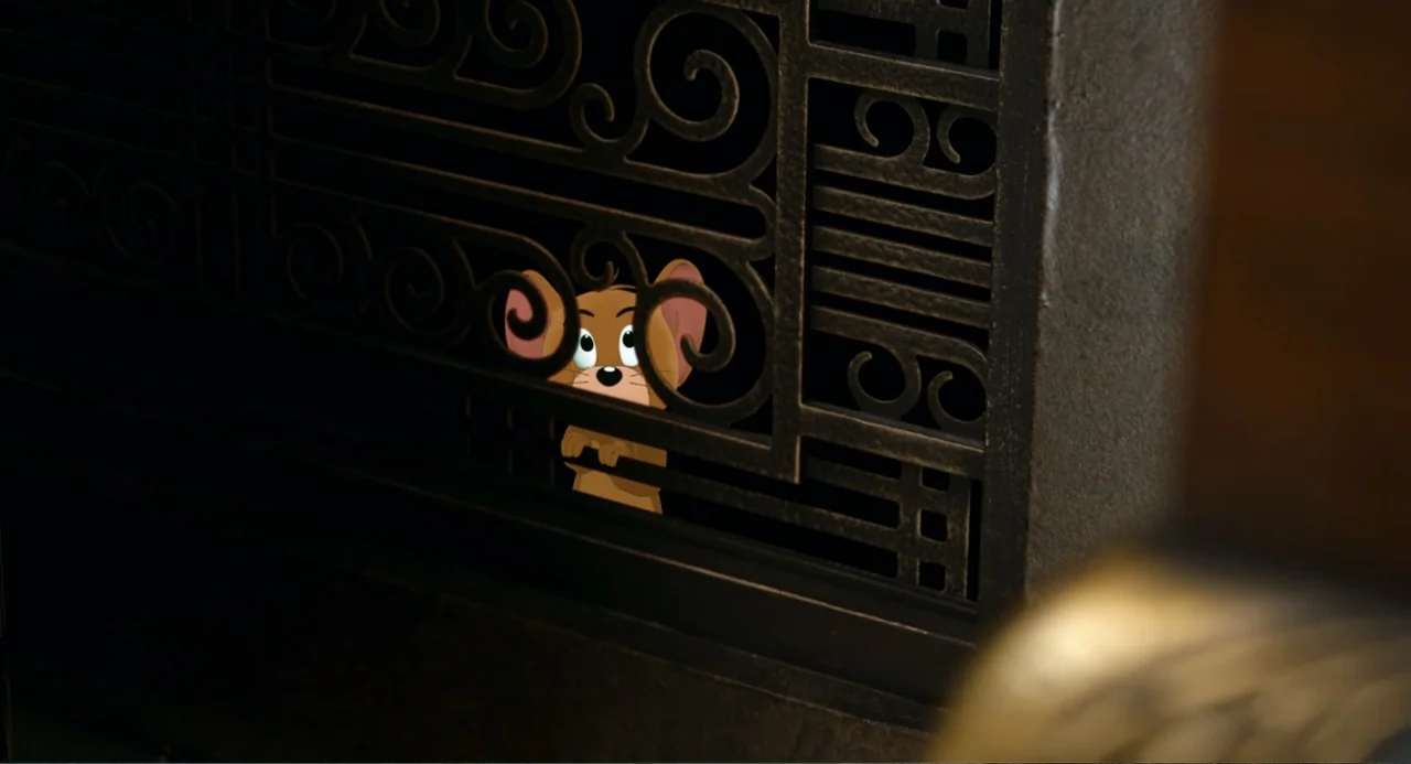 Tom & Jerry (2021) movie still: closeup — A dark fireplace interior features an intricate, black, wrought-iron screen with ornate geometric…