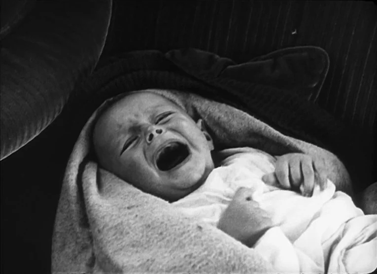 The Kid (1921) movie still: closeup — A dark environment with an infant lying on a velvet cushion. The baby is wrapped in a light-colored blanket…