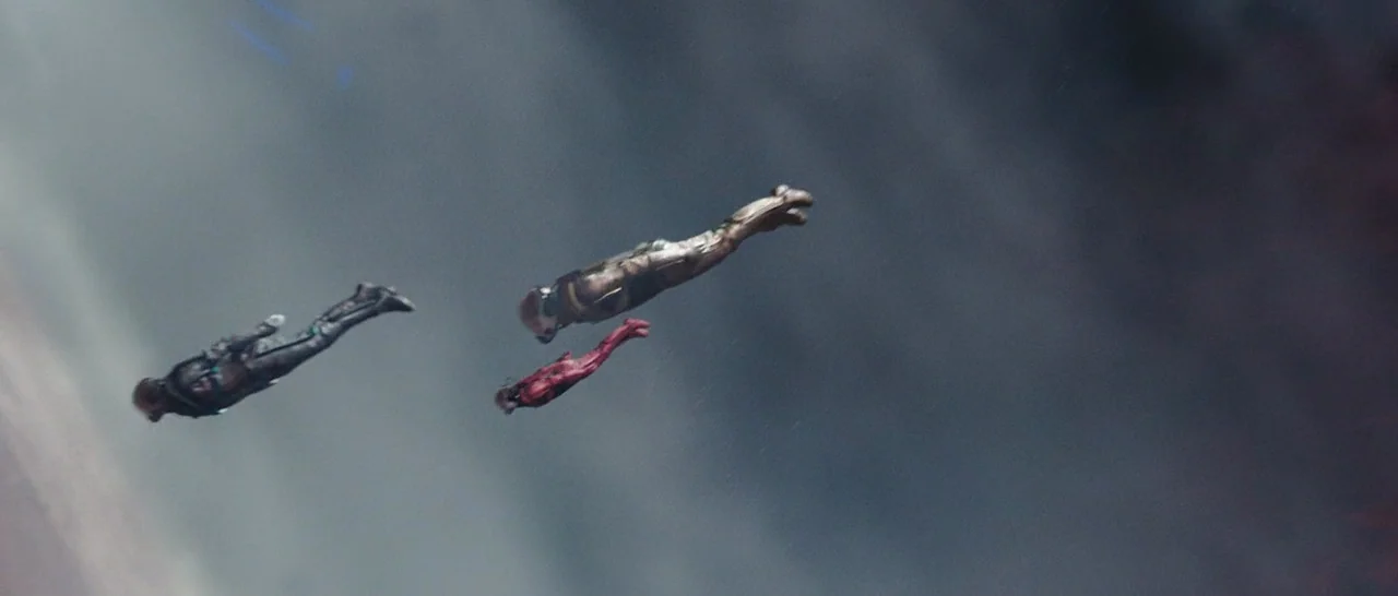 Star Trek (2009) movie still: wide — Three individuals in specialized flight suits drift horizontally against a vast, overcast sky. The figures are…