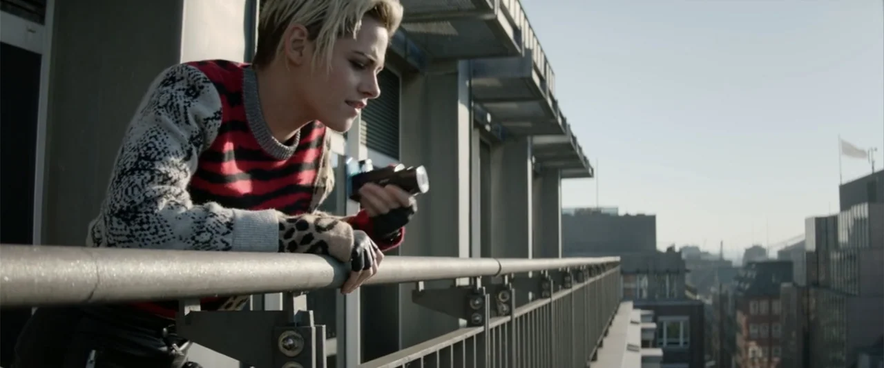 Charlie's Angels (2019) movie still: medium — A modern building balcony overlooks a blurred city skyline during the day. A woman in a patterned…