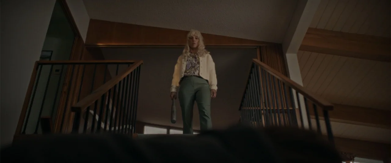Silent Night, Deadly Night (2025) movie still: fullbody — A split-level residential interior with wooden paneling and a dark railing leading to…