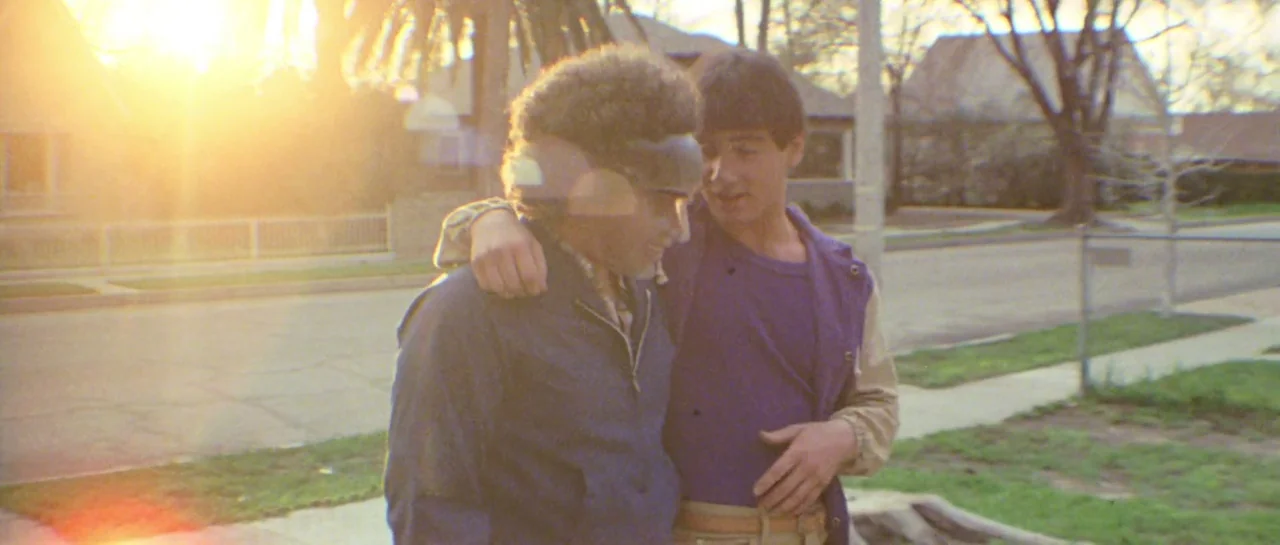 Friday the 13th Part III (1982) movie still: medium — Two teenagers stand on a suburban sidewalk during a bright golden hour sunset. They have their…