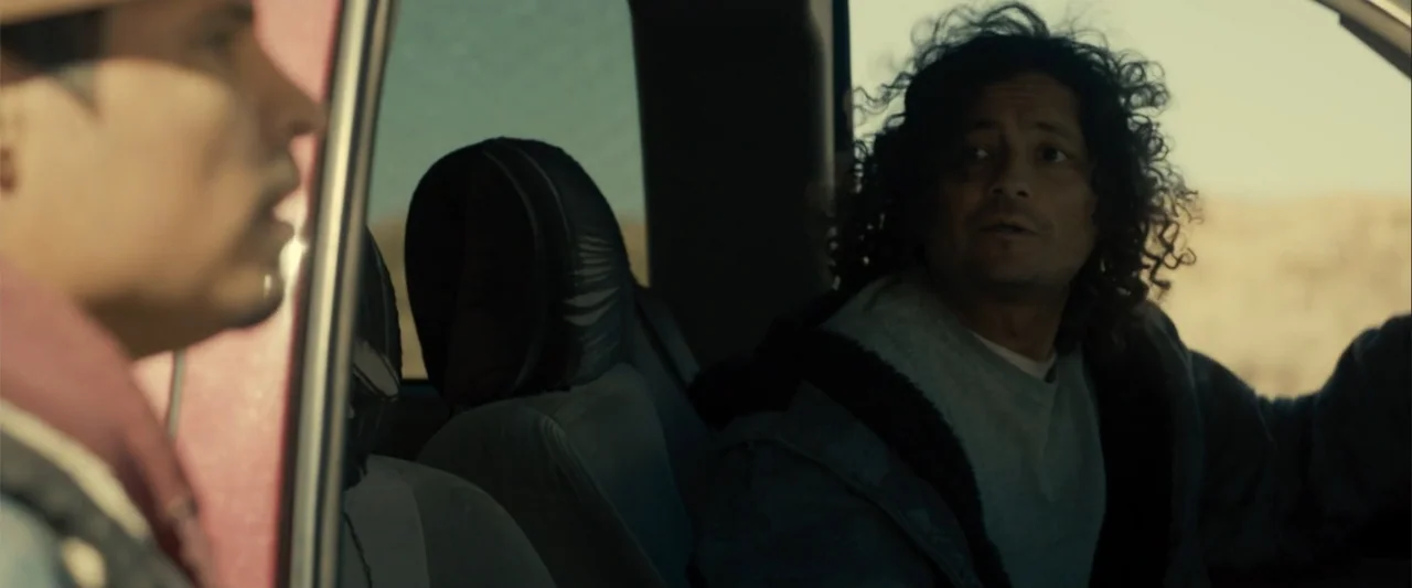 Frontera (2014) movie still: medium — The interior of a moving vehicle displays two men seated in the front. One man looks towards the driver while…