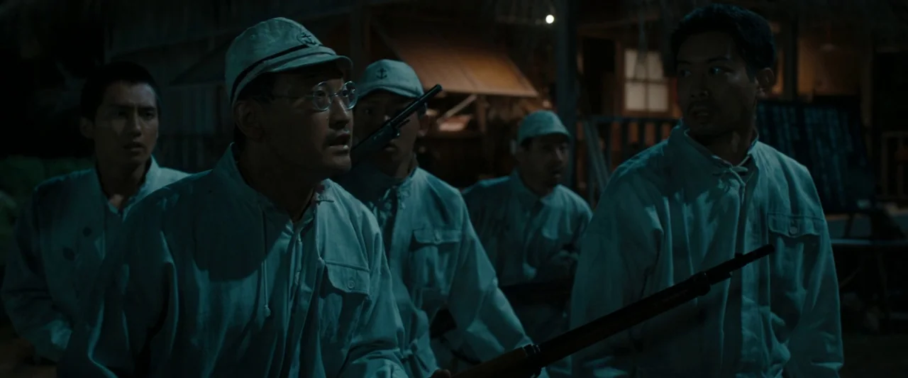 Godzilla Minus One (2023) movie still: medium — A group of soldiers in light-colored uniforms stands in a dark outdoor encampment at night. They…