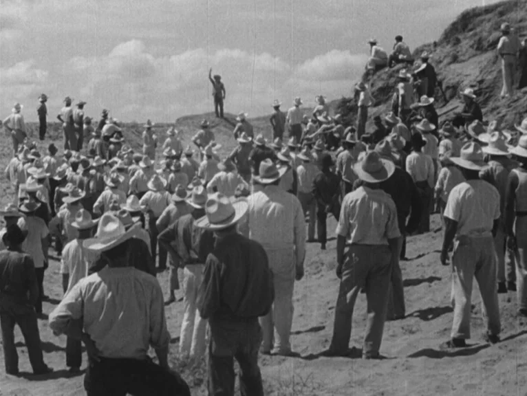 Redes (1936) movie still: wide — A large crowd of men wearing hats stands on a sunlit sand dune. One man in the distance gestures upward while the…