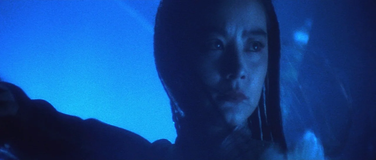 The Bride With White Hair (1993) movie still: closeup — A dark, indistinguishable interior is bathed in an intense blue light. A woman stands in the…