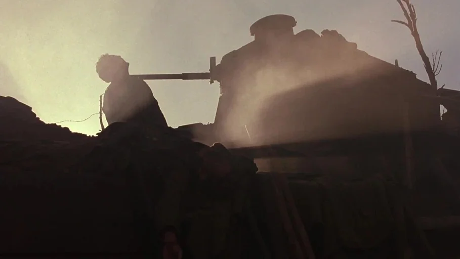 A Little Princess (1995) movie still: wide — A war-torn exterior landscape features a heavy tank silhouetted against a bright, hazy sky. Thick smoke…
