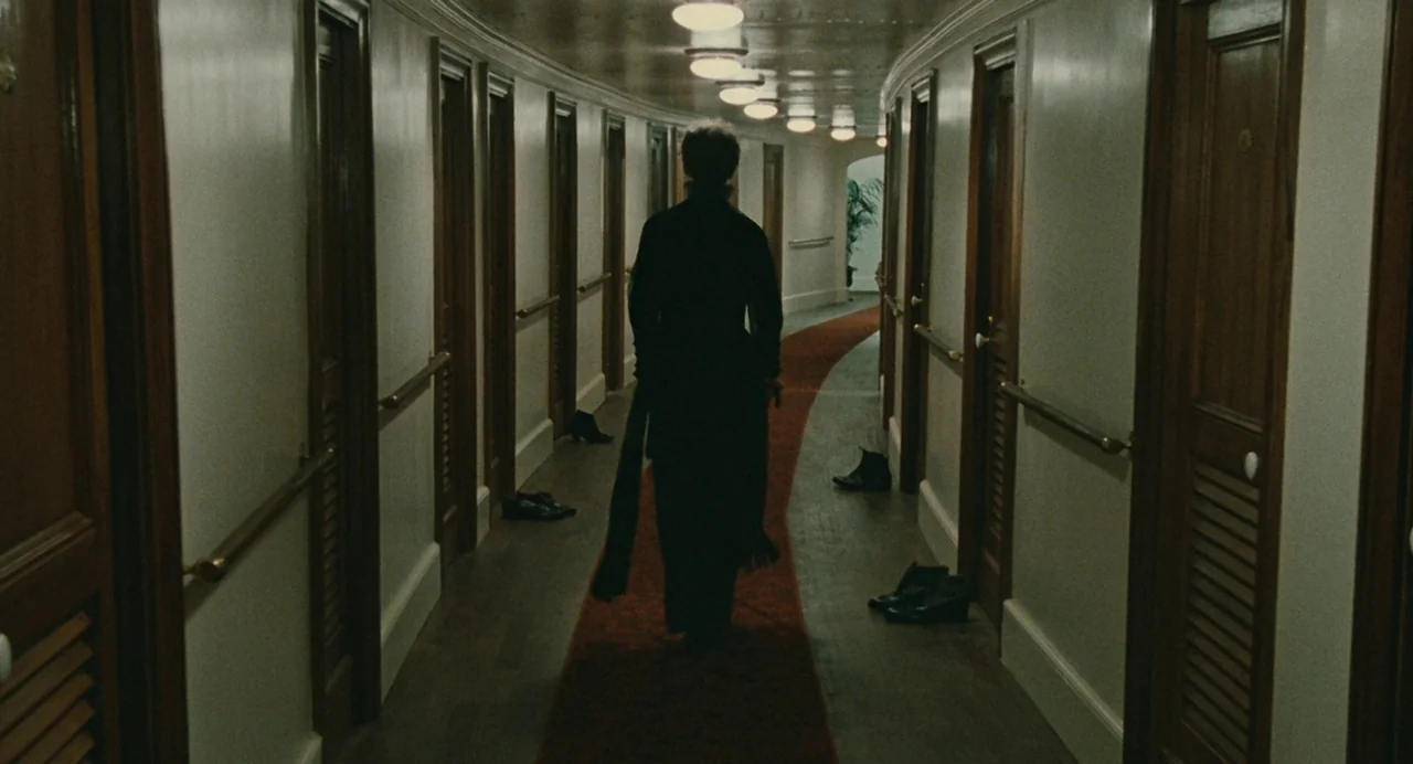 And The Ship Sails On (1983) movie still: fullbody — A long ship hallway features a central red carpet flanked by uniform wooden doors. A lone…