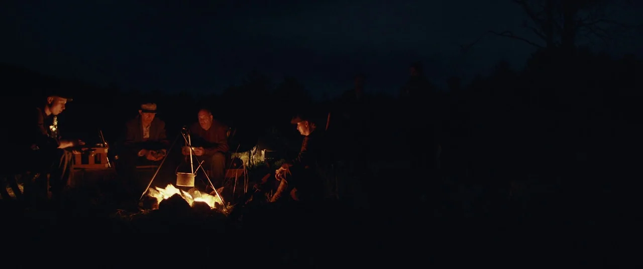The Man Who Killed Hitler and Then the Bigfoot (2018) movie still: wide — A group of men sit around a campfire in a dark wooded area at night. They…