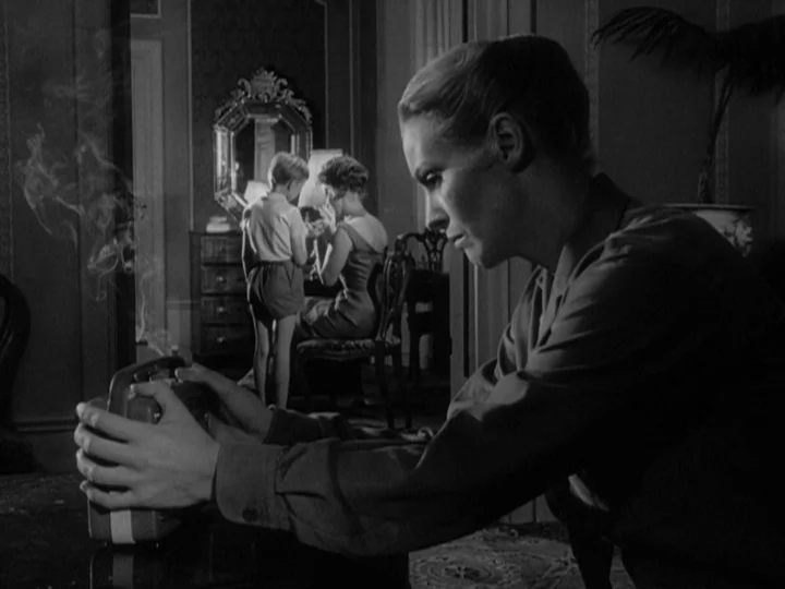 The Silence (1963) movie still: medium — An interior space features a foreground woman manipulating a smoking electronic device. In the background a…